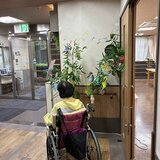 スーパーコート高石羽衣の玄関エントランスにて、七夕の笹飾りの前で記念撮影をする車椅子に乗ったご入居者の後ろ姿。