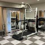 スーパーコート高石羽衣のリハビリルームにある、白いフレームの免荷装置と一体化したトレッドミル。清潔な空間と大きな鏡が写っている。