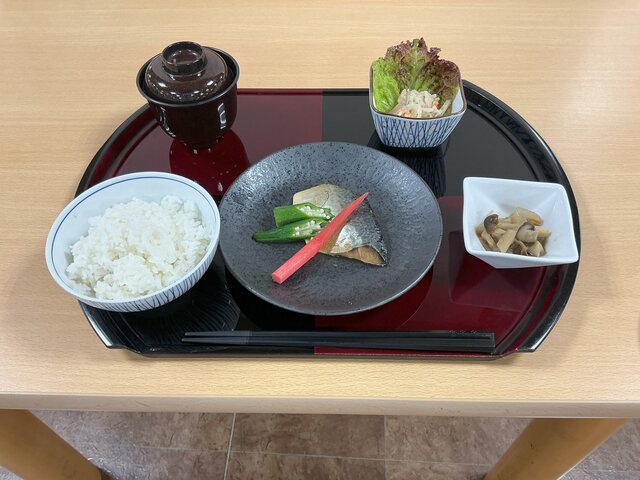 alt="スーパーコート高石羽衣の夕食「プライムメニュー」。黒と赤のお盆に、白ご飯、お味噌汁、主菜の鯖の柚庵焼き（オクラとはじかみ生姜添え）、副菜のきのこのソテー、切り干し大根とハムのサラダが綺麗に並べられた和食セットの様子。"