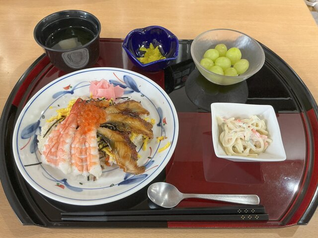 スーパーコート高石羽衣で提供されたごちそうメニュー。お盆の上に置かれた、鰻・海老・いくらが贅沢に乗った彩り豊かなちらし寿司、スパゲティサラダ、清汁、漬物、デザートのマスカット。