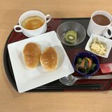 スーパーコート高石羽衣の朝食「プライムメニュー」。トレイに載った2個のロールパン、コンソメスープ、ほうれん草のソテー、玉子サラダ、キウイフルーツ、カップに入った飲み物。
