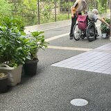 スーパーコート高石羽衣の敷地内で、車椅子に乗ったご入居者がスタッフに見守られながら、ハイビスカスの鉢植えに一生懸命手を伸ばして水やりをしている様子