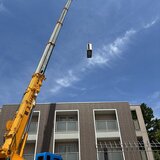 スーパーコート高石羽衣の建物前に配置された黄色い大型クレーン車と吊り上げられるエアコン室外機