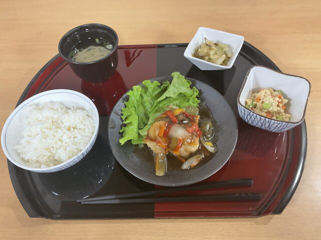 スーパーコート高石羽衣の夕食「プライムメニュー」の配膳写真。黒と赤のお盆の上に、メインの赤魚の甘酢あんかけ、ご飯、清汁、炒り豆腐、キャベツの塩昆布和えが綺麗に並んでいる。