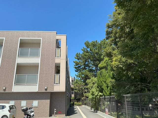 alt="澄み渡る青空と緑豊かな樹木に隣接する有料老人ホーム「スーパーコート高石羽衣」の外観"