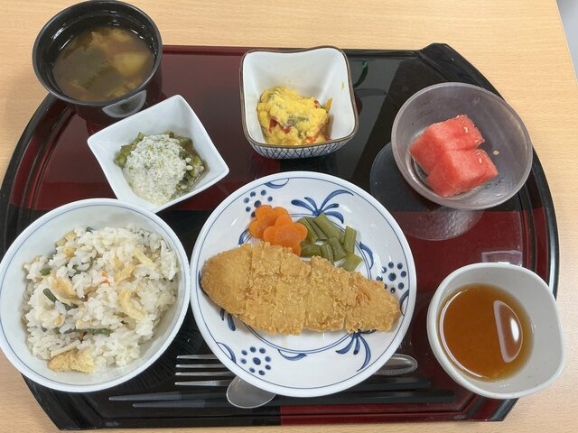 お膳に乗ったスーパーコート高石羽衣の「山の日」イベント食。手前にわらびと筍の炊き込みご飯と鶏天の皿（人参とインゲン添え）。奥に赤出汁、オクラとろろ、黄色いピーマンの炒め物、スイカが並ぶ。