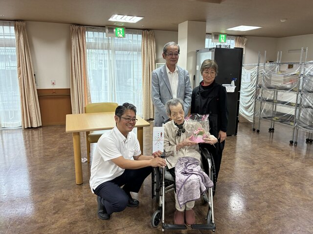 alt="スーパーコート高石羽衣にて敬老の日・100歳のお祝いで高石市長からお花と祝い箸を贈られ記念撮影をするご入居者様"
