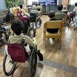 スーパー・コート高石羽衣の2階談話室で、モニターの映像を見ながら車椅子や椅子に座って午後の体操に参加するご入居者様の様子