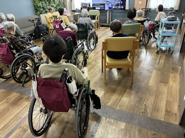 スーパー・コート高石羽衣の2階談話室で、モニターの映像を見ながら車椅子や椅子に座って午後の体操に参加するご入居者様の様子