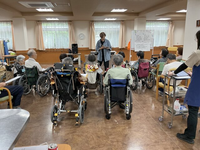 alt="スーパーコート高石羽衣の食堂でうめづ音楽教室の梅津先生がホワイトボードの前で音楽療法レクリエーションを行う様子"