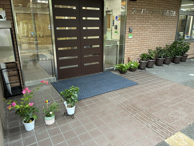 alt="大雨に備えてエントランスの軒下に避難された鉢植えの花と、スーパー・コート高石羽衣の玄関"
