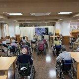 スーパーコート高石羽衣で昨日行われたストレッチ体操の様子。デイルームにて、正面のモニターとスタッフに合わせてご入居者が無理のない姿勢で体を動かしている風景。