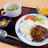 スーパーコート高石羽衣で提供された「ごちそうメニュー」のセット。黒と赤の和風トレイに、ご飯の上にハンバーグ、目玉焼き、アボカド、トマトが盛られたロコモコ丼、小さな鉢に入ったキャベツの青ドレ和え、コンソメスープ、ガラスボウルに入ったカットオレンジが並んでいる。