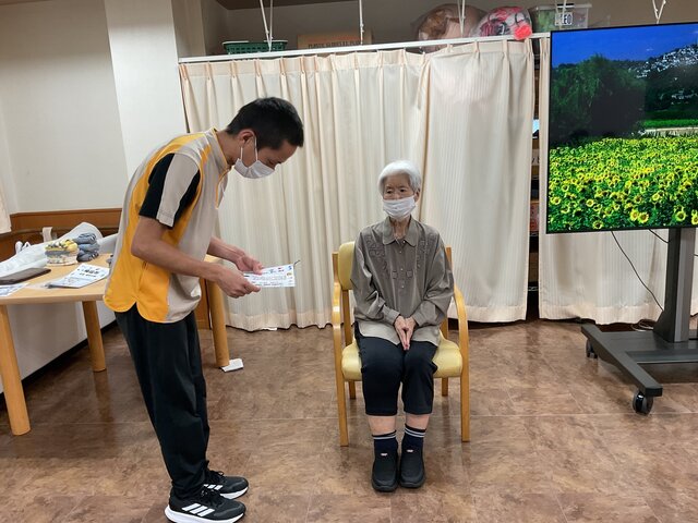 体操キャンペーン表彰式にて、スタッフから表彰状と記念品を受け取るご利用者様の様子