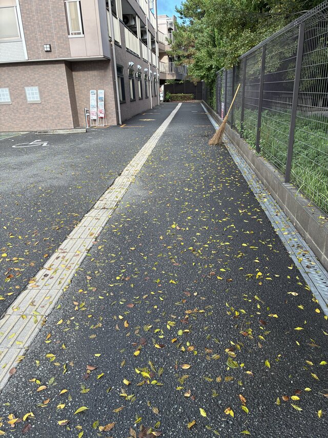 alt="雨と強風が去った翌朝、スーパー・コート高石羽衣の玄関前通路に一面に広がった落ち葉と立てかけられた竹箒"