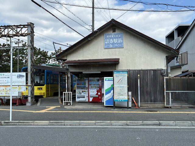 alt="阪堺電気軌道阪堺線の浜寺駅前停留場のレトロな木造駅舎と、ホームに停車中の黄色と青の路面電車"