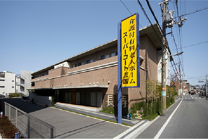 介護施設の建物外観。黄色い看板が目印で、入り口に向かう車寄せが見える。